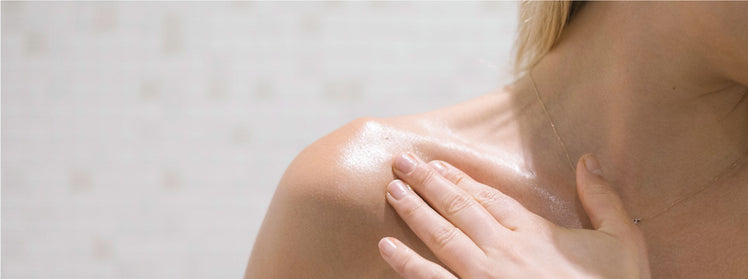 A person applying body oil to their shoulder