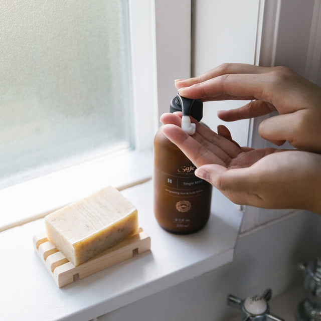 Hands dispensing lotion from the bottle, next to a bar of soap and a window