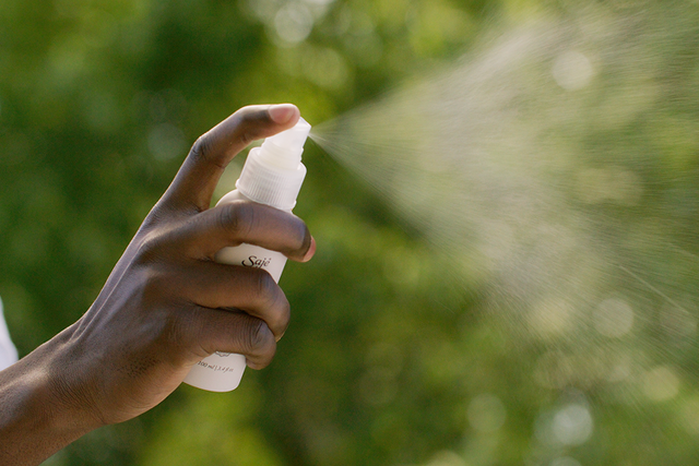 A woman applying a roll-on to her neck against a blue sky