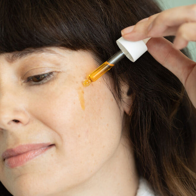 A woman dropping True Dew Face Oil onto her cheek