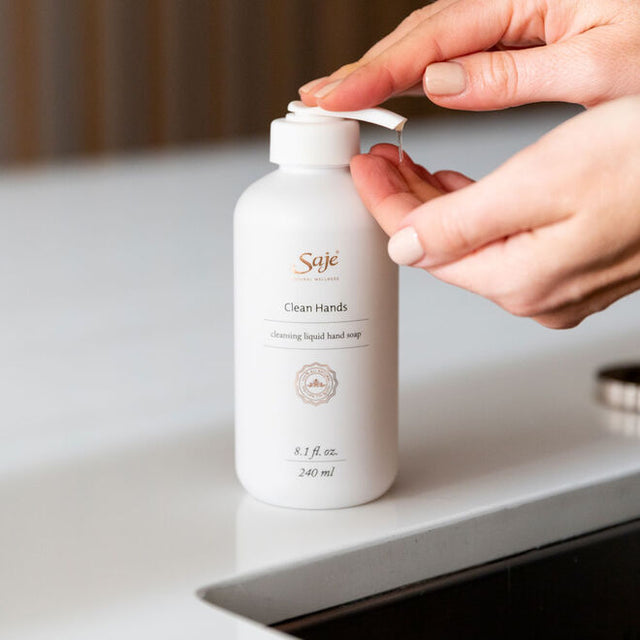A pair of hands dispensing liquid hand soap into its other hand by a sink 