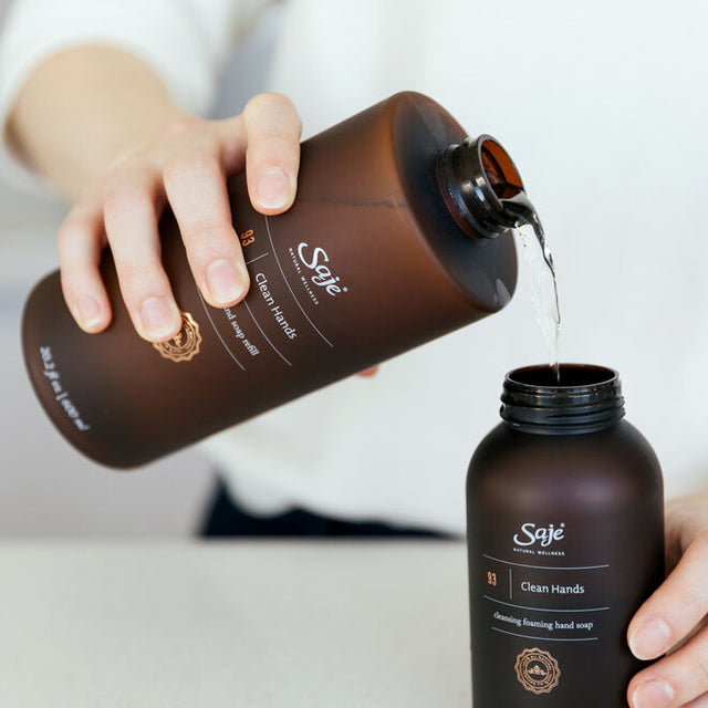 A pair of hands refilling the Clean Hands foaming hand soap dispenser from the refill bottle