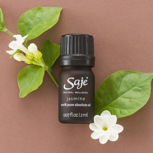 flatlay of a bottle of pure jasmine essential oil beside jasmine flowers