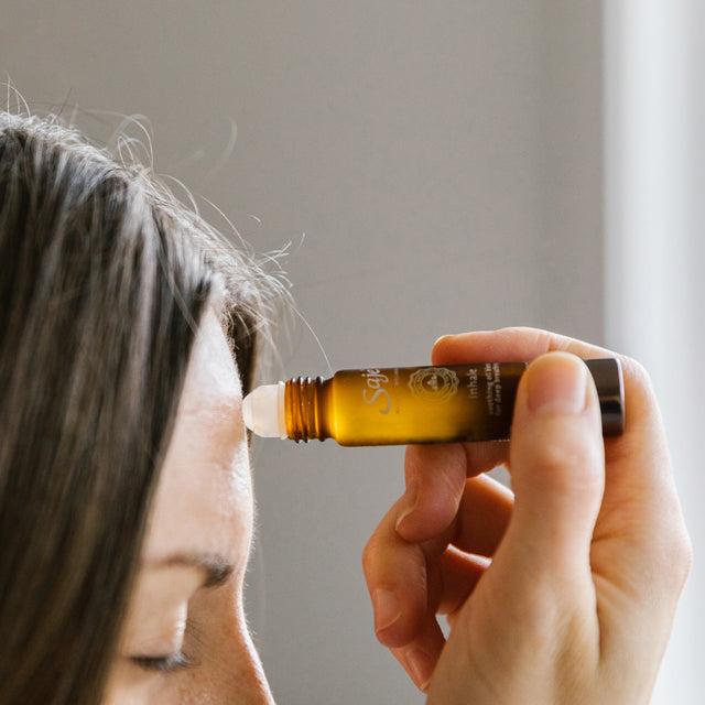 A woman applying Inhale soothing oil blend roll-on 0.34 fl oz onto their forehead 