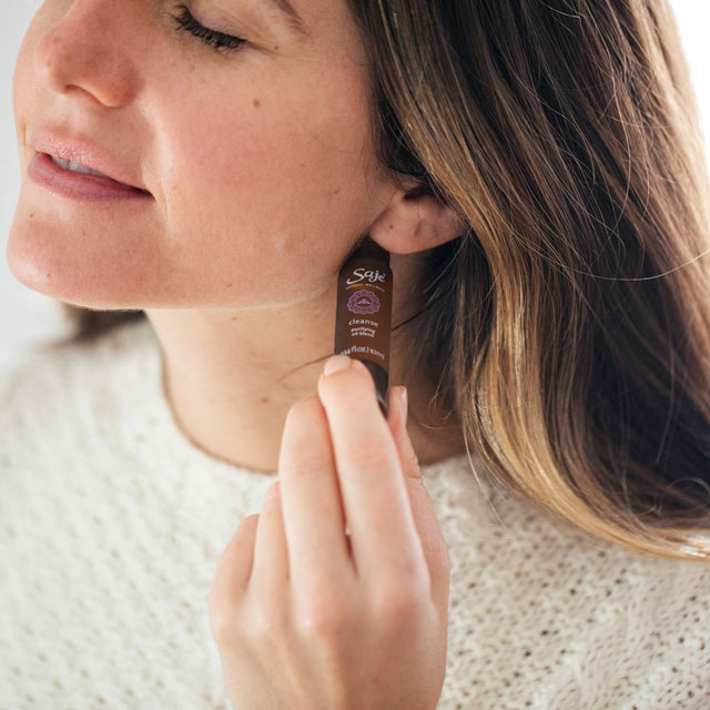 a woman with her eyes closed using Cleanse roll-on on her neck while wearing a cream sweater