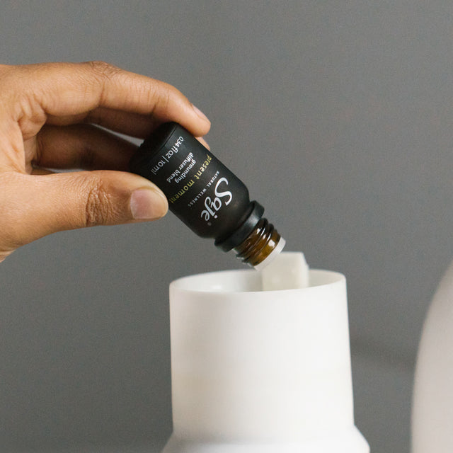 A hand putting Present Moment diffuser blend into a diffuser water tank