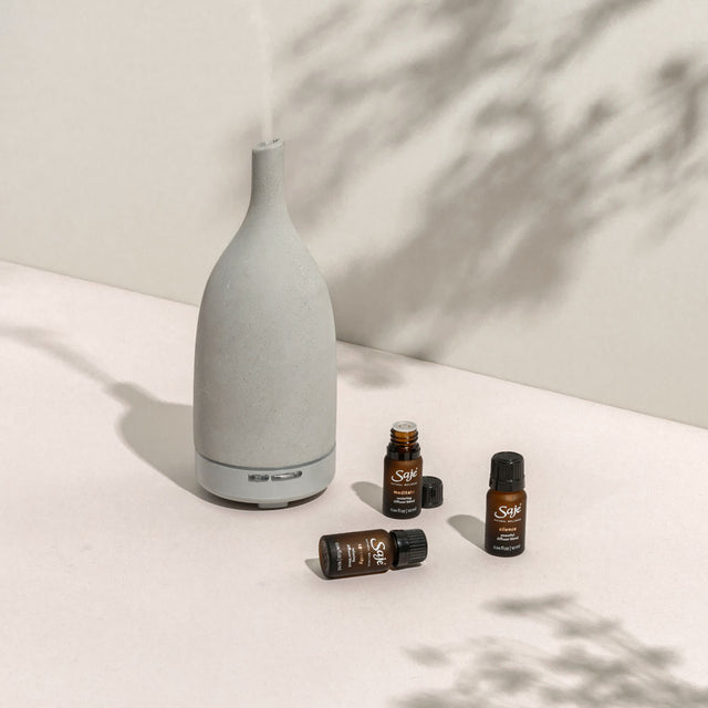 Aroma Om stone diffuser with diffuser blends beside it on a moody background