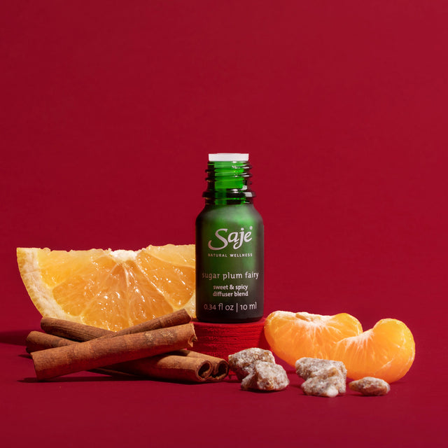 Sugar Plum Fairy Diffuser Blend bottle with the cap off beside tangerine and cinnamon sticks on a red background